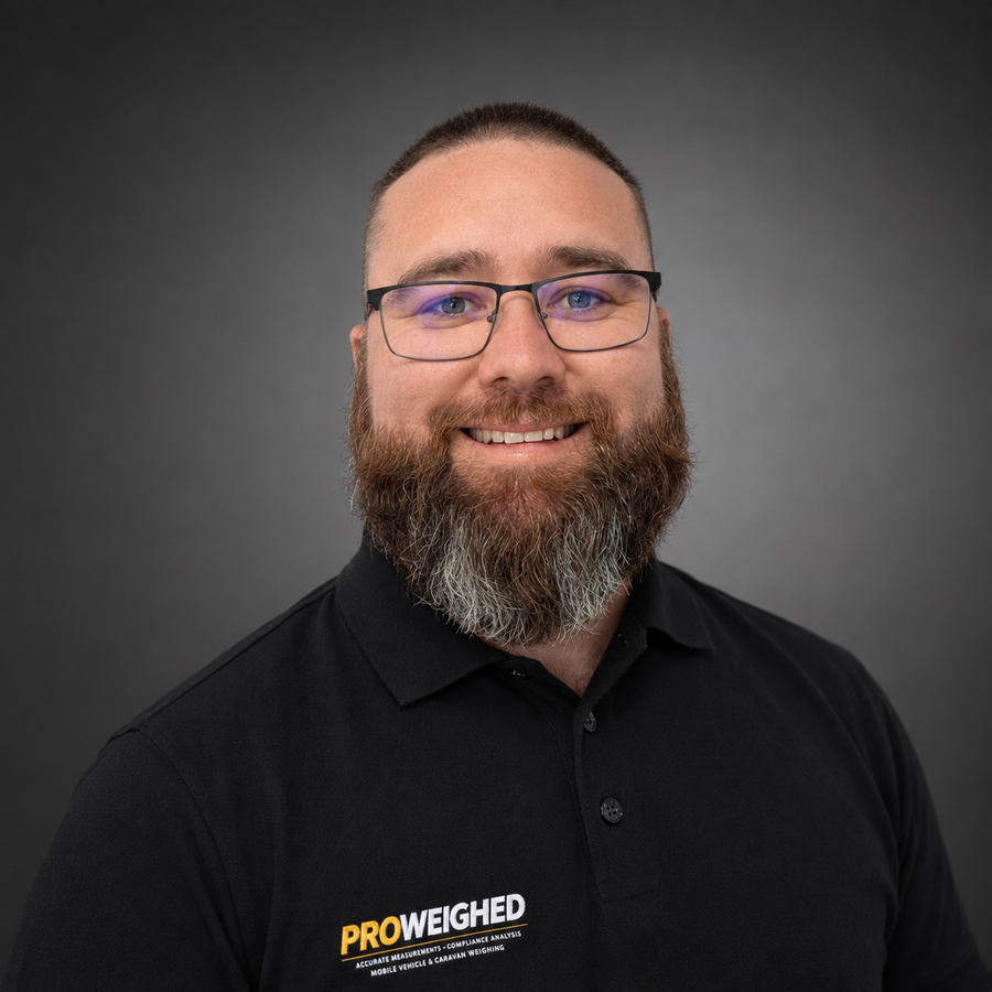 A smiling man with a beard and glasses wearing a black polo shirt with the 'PROWEIGHED' logo on the left chest, set against a dark gray studio background.