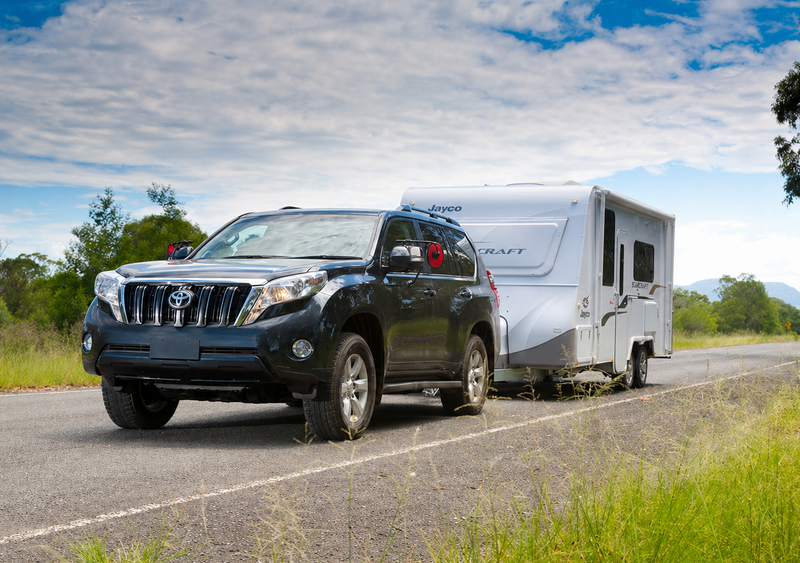 Black SUV towing a white travel trailer on a road with trees and blue sky in the background