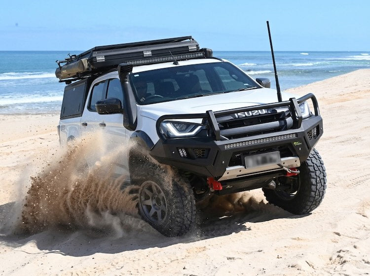 Isuzu truck driving on a sandy beach with ocean in the background